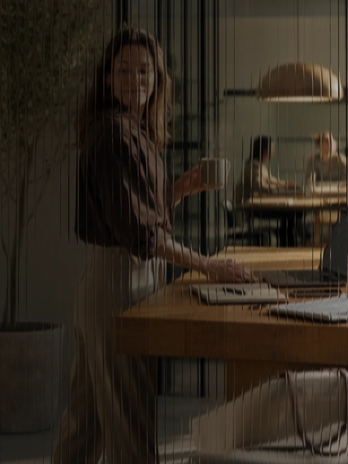 A woman at an oak counter glancing at her laptop before heading into a meeting, seen through fluted glass