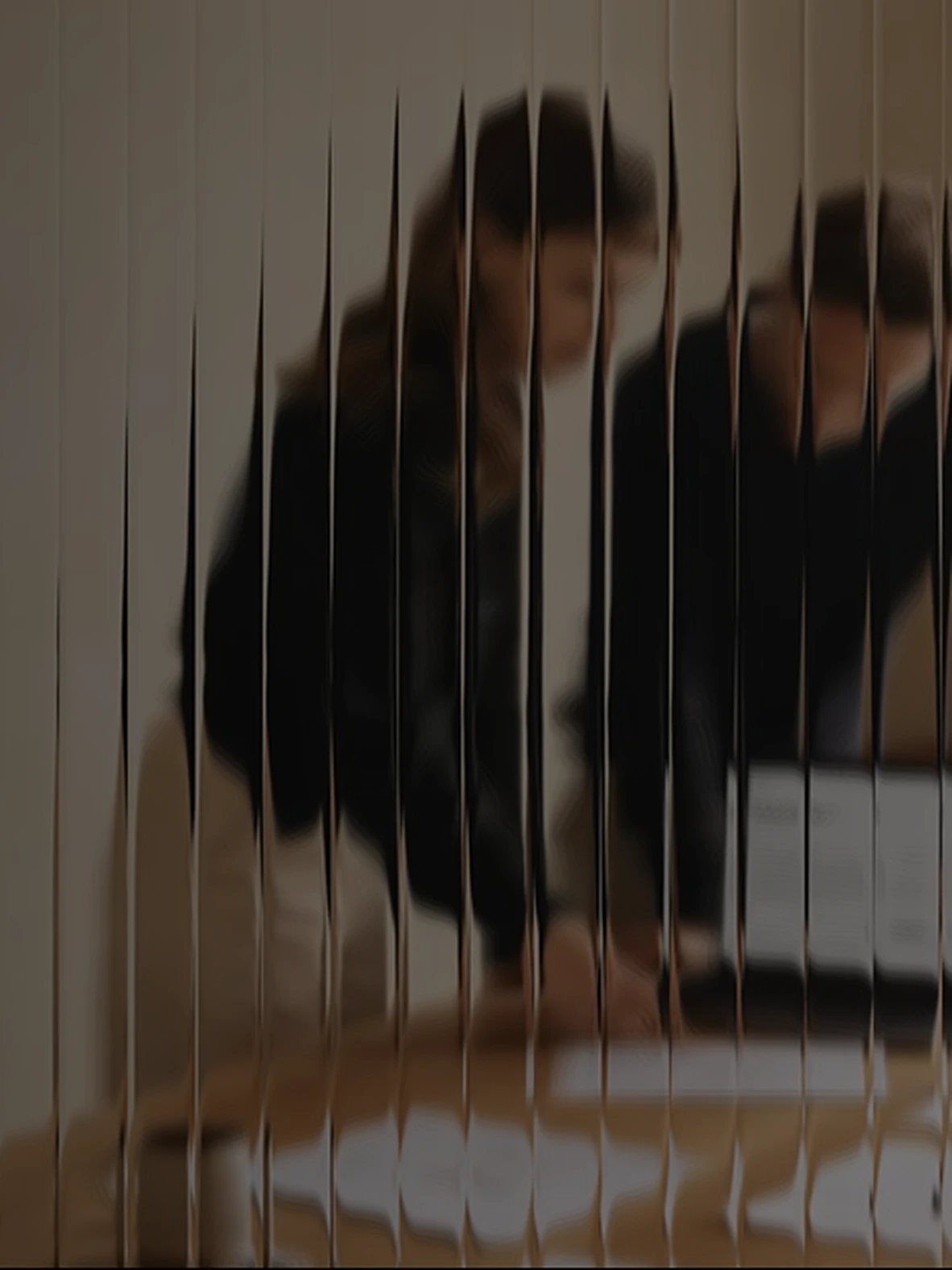 Two colleagues at a desk reviewing a laptop together, seen through fluted glass