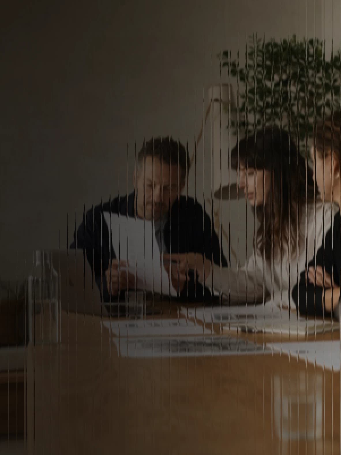 Three colleagues at a table reading through a CV, seen through fluted glass
