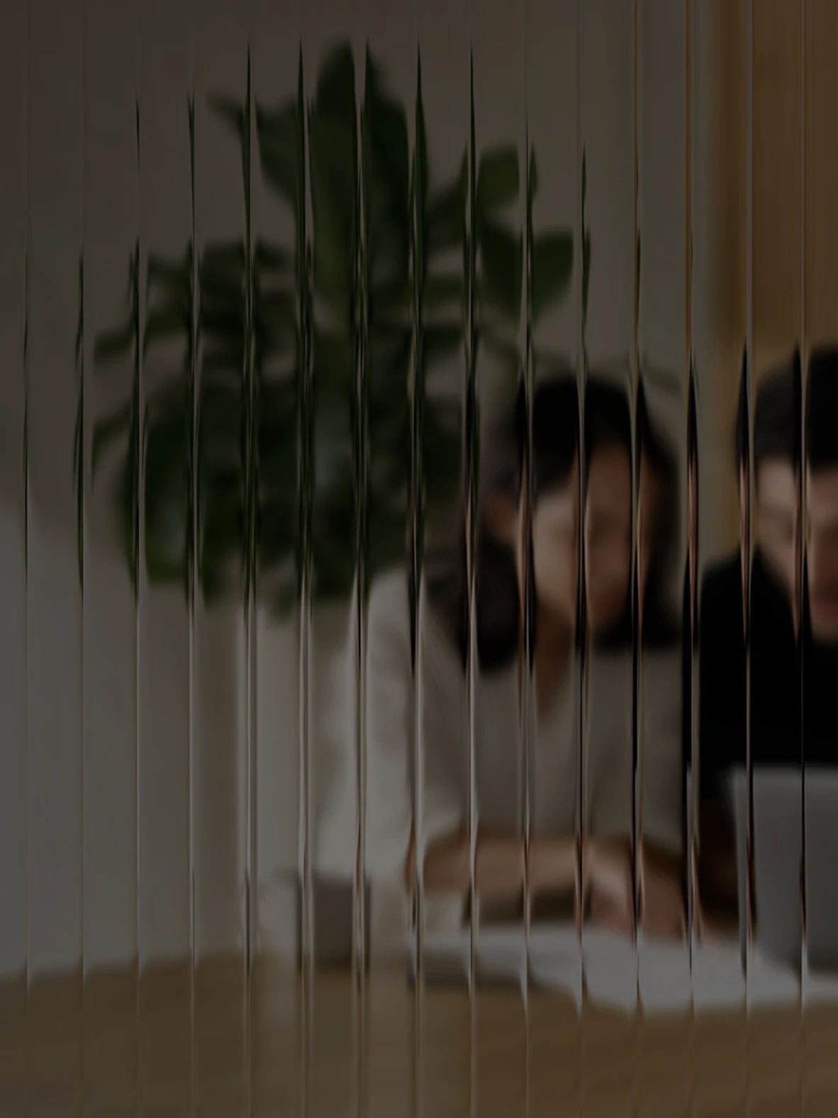 Three colleagues around a laptop at a desk, seen through fluted glass